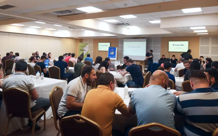 Indoor event with attendees at round tables for a "JS Jungle Quiz" displayed on two screens